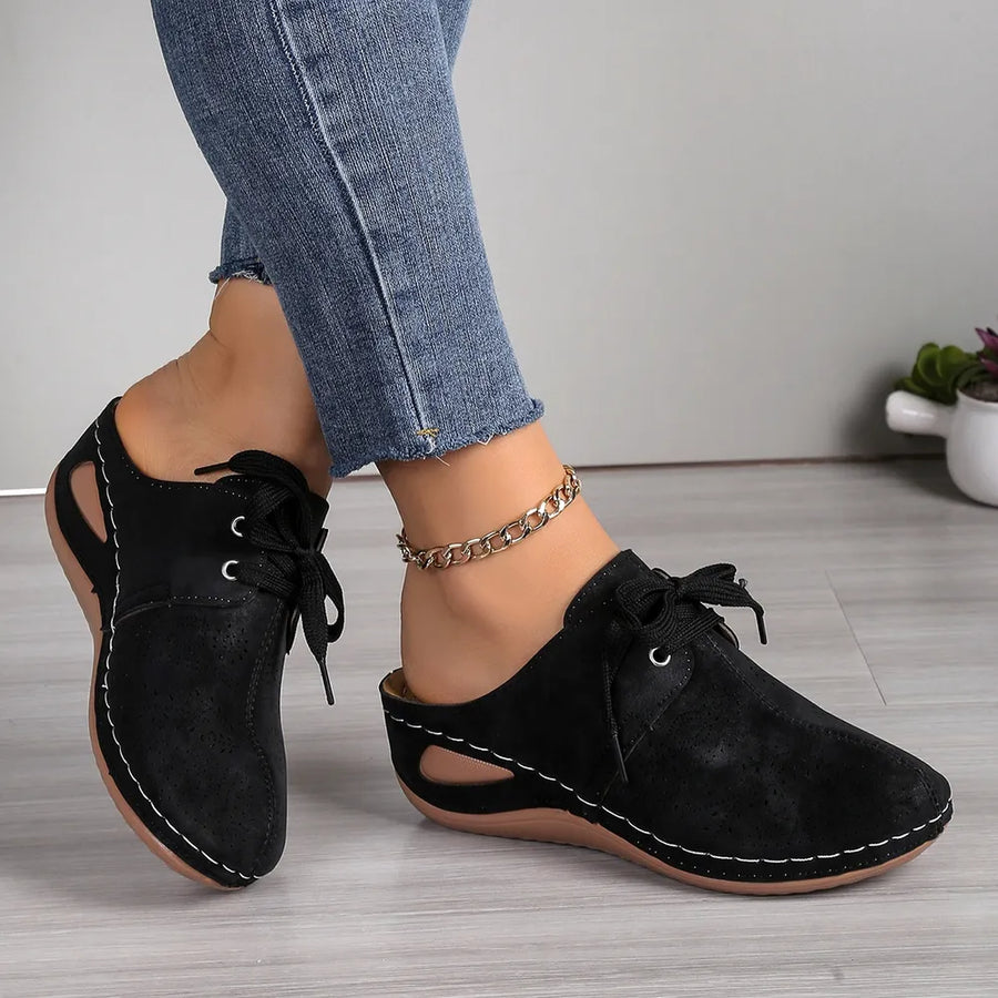 Black perforated lace-up mule flats with white stitching and cut-out sides.