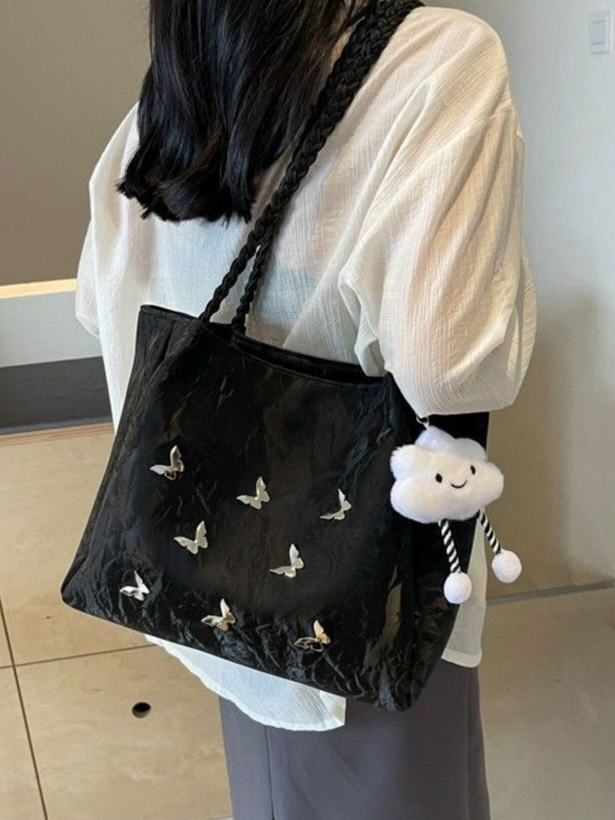 Black shopper bag with braided handles, butterfly details, and cloud charm.