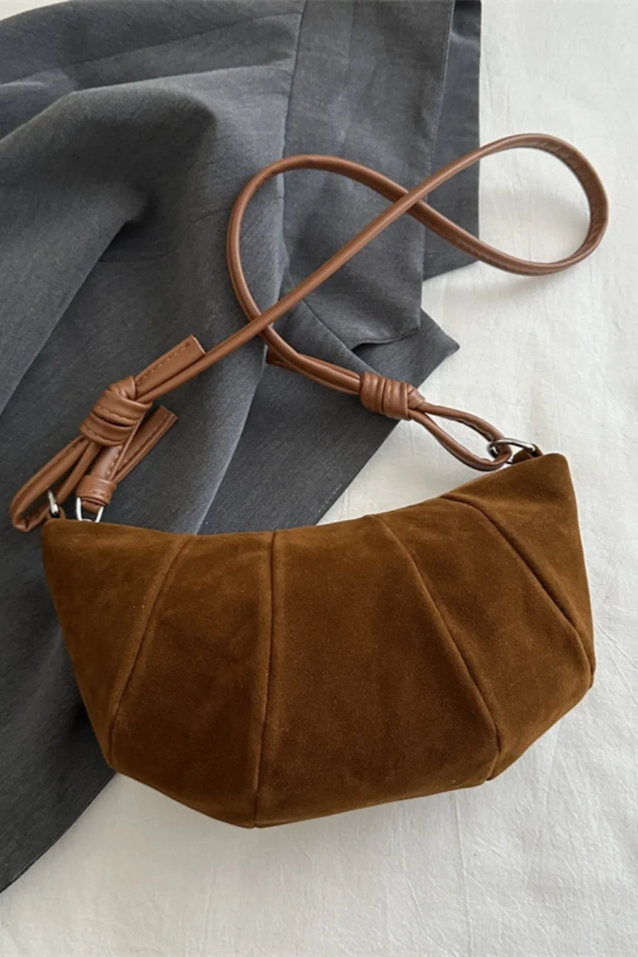 Brown suede crescent shoulder bag with pleated detail and knotted strap.