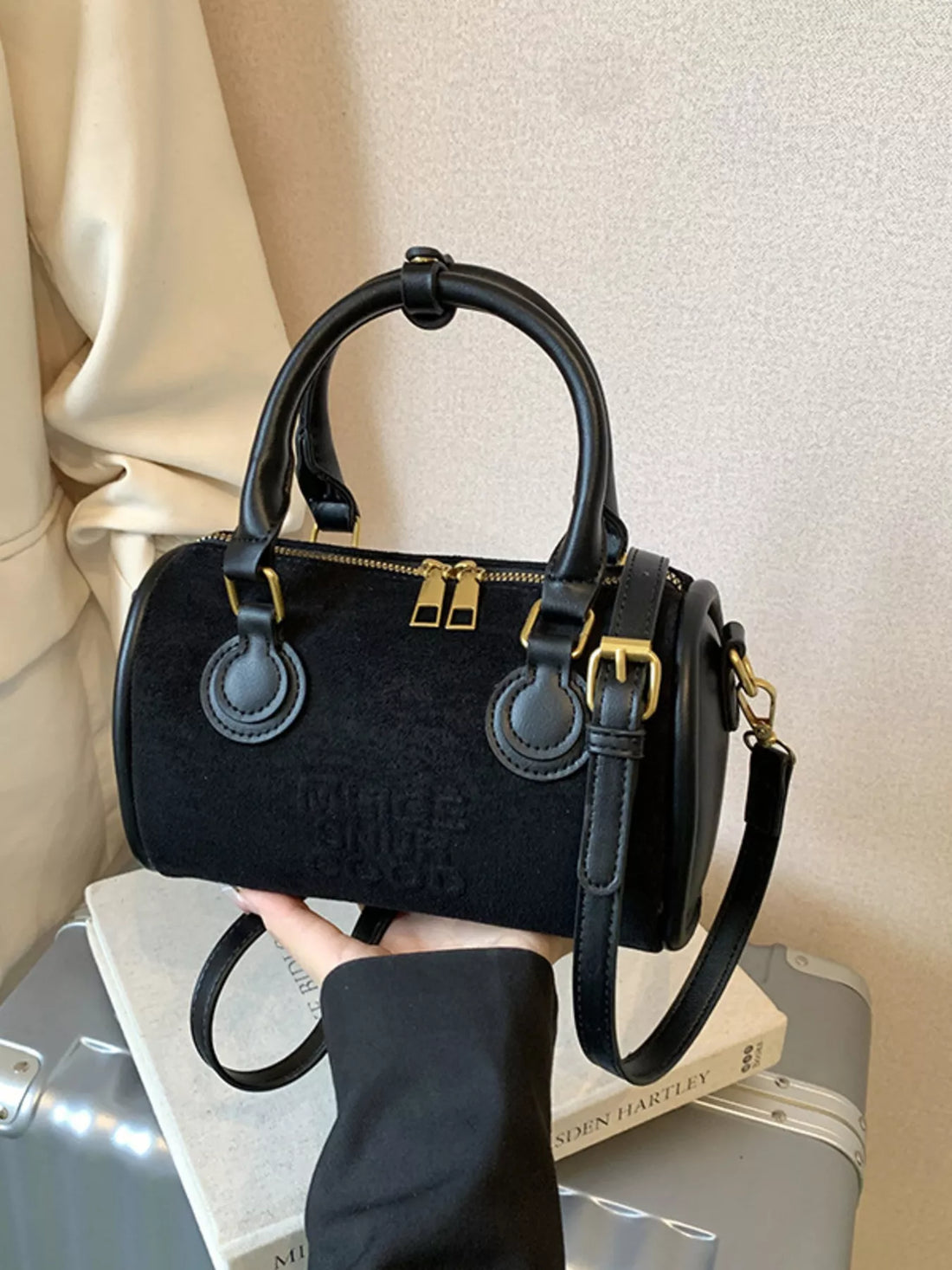 Small black barrel crossbody bag with gold hardware and embossed logo
