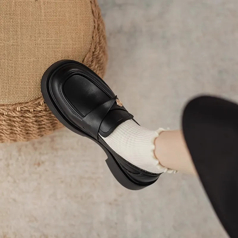 Black penny loafers with gold detail and a thick sole, styled with white ruffled socks.