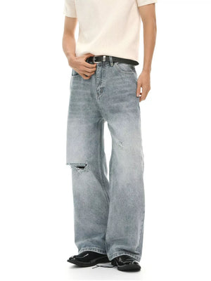 Men's light wash distressed wide-leg denim jeans with a ripped knee detail.