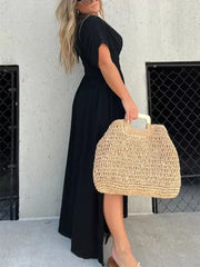 Black V-neck maxi dress with dolman sleeves and smocked waist, worn with a straw bag.
