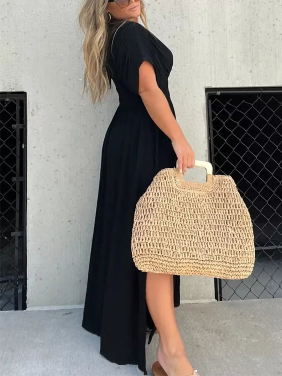 Black V-neck maxi dress with dolman sleeves and smocked waist, worn with a straw bag.