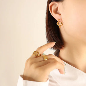 Gold Star huggie earrings in steel, worn by a woman with gold rings.