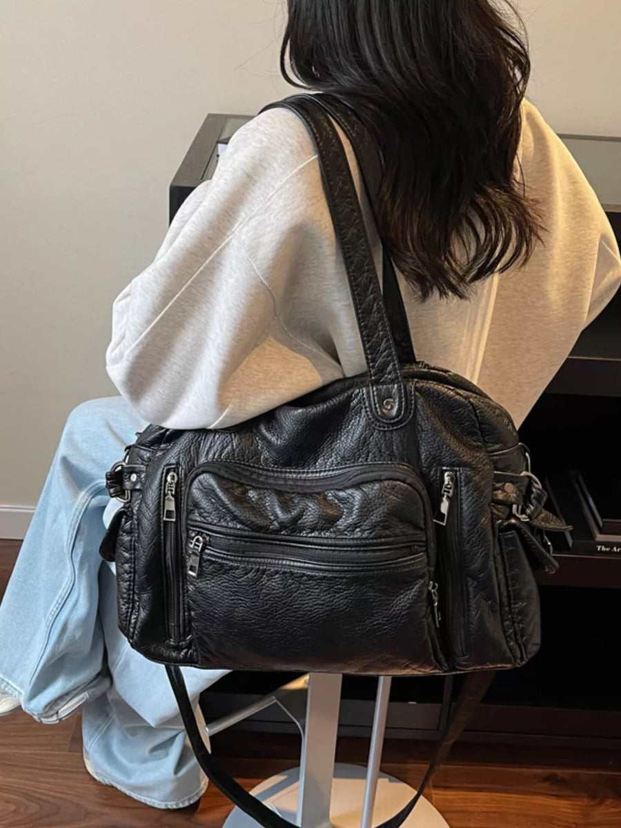 Black pebbled leather crossbody bag with multiple zippered pockets and adjustable strap.