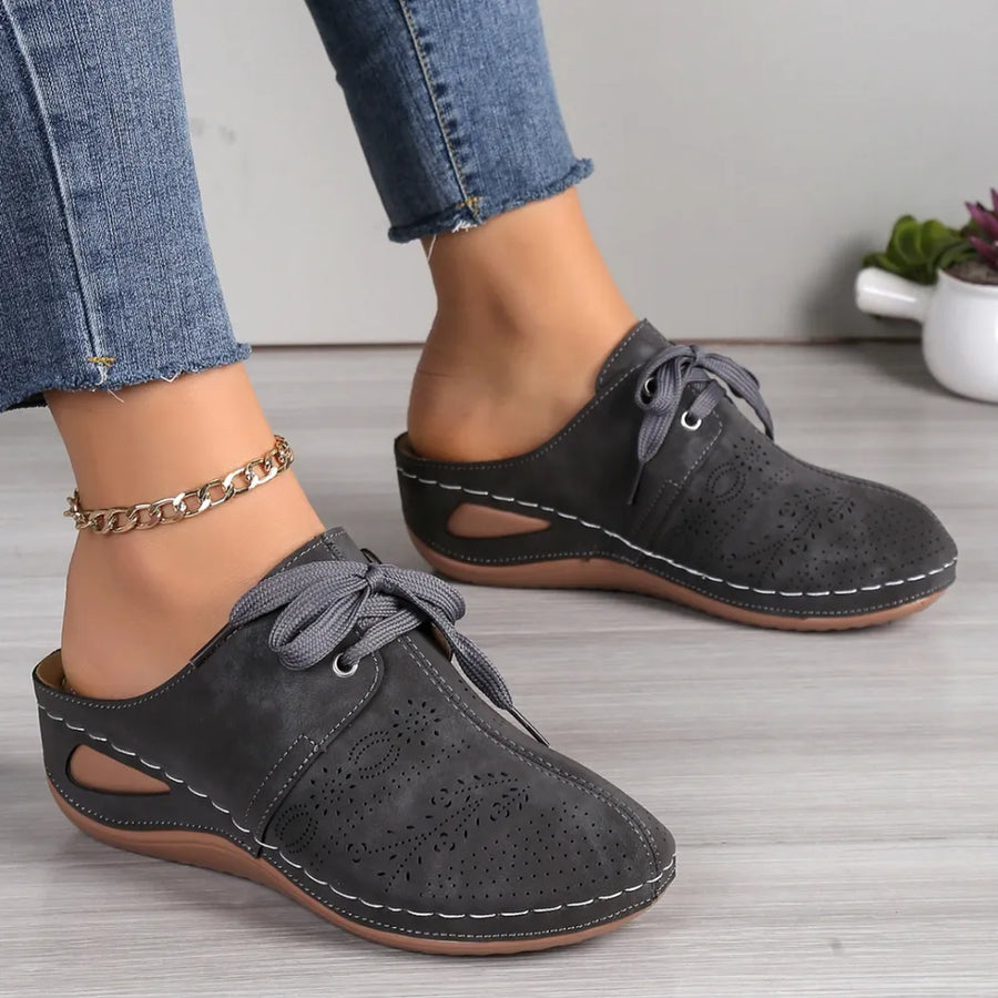 Dark gray perforated lace-up mule flats with white stitching and cut-out sides.
