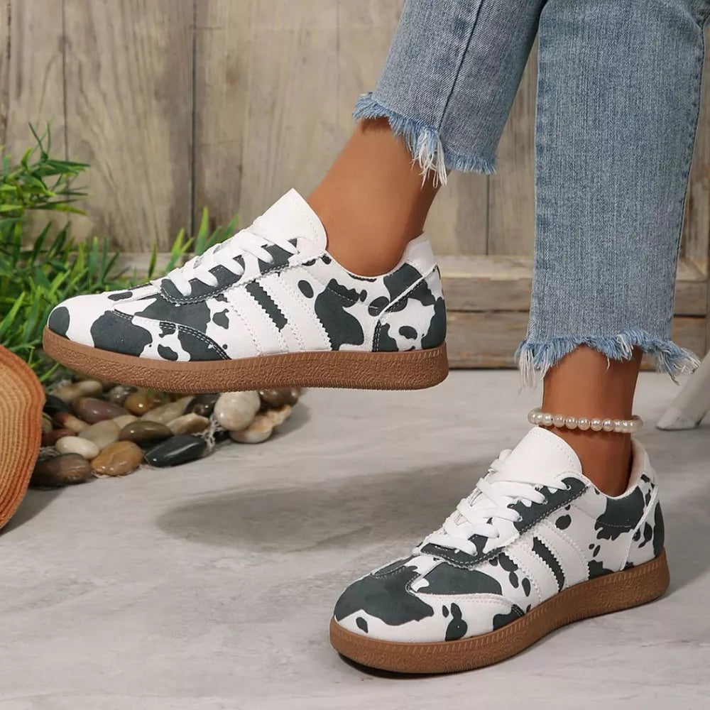 Trendy cow print low-top sneakers with white and black pattern and brown sole.