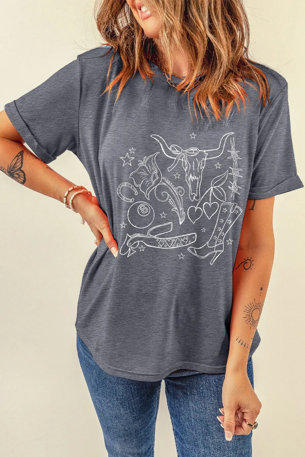 Gray graphic t-shirt with western tattoo print, featuring a bull skull, boots, and hearts.