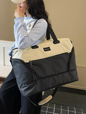 Textured two-tone large duffle bag in black and cream with adjustable strap and zippered pockets.