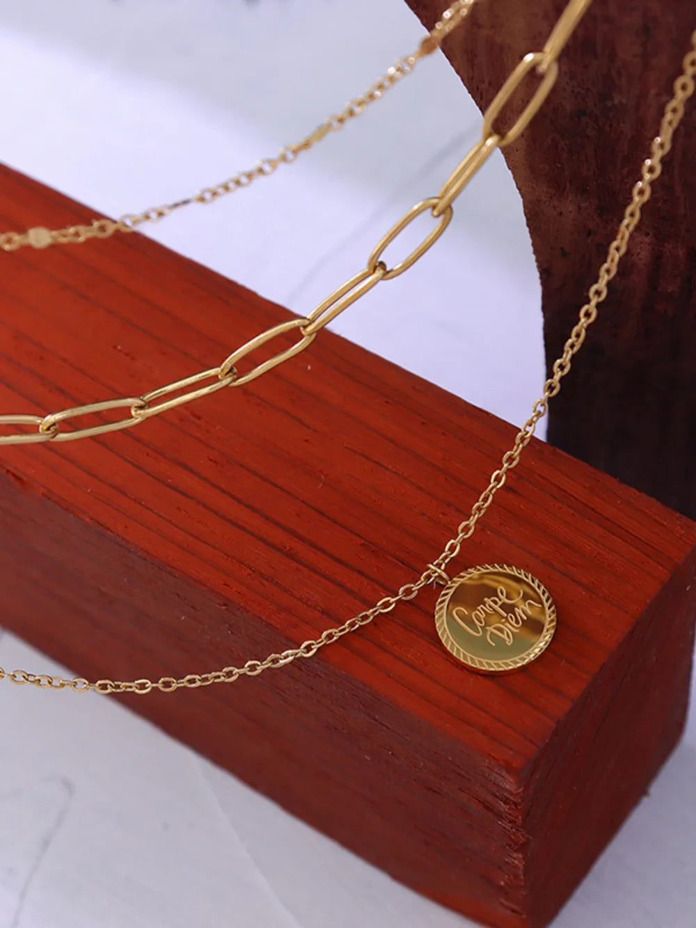 Gold layered chain necklace with "Carpe Diem" pendant and paperclip chain detail.