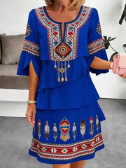 Blue boho tiered dress with embroidered neckline, sleeves, and hem featuring feathers and geometric patterns.