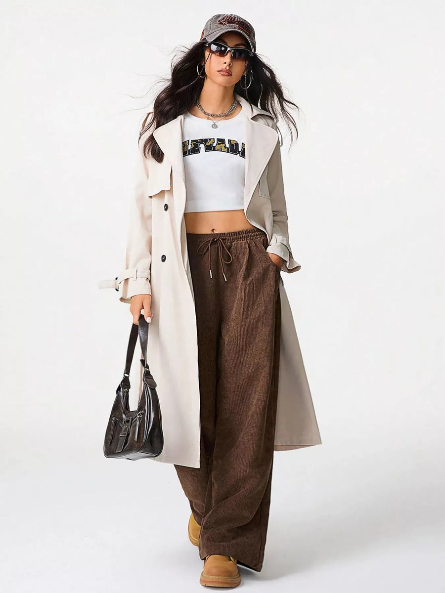 Brown corduroy drawstring pants with a relaxed fit and wide leg, styled with a crop top and trench coat.