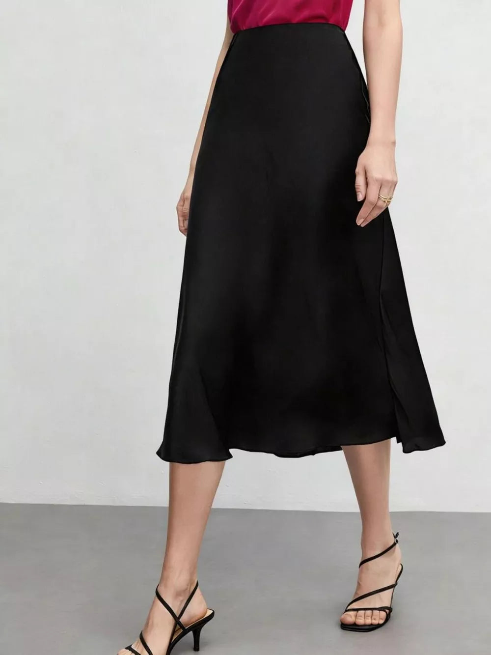 Elegant black high-waisted A-line midi skirt with a subtle side slit, styled with strappy heels.