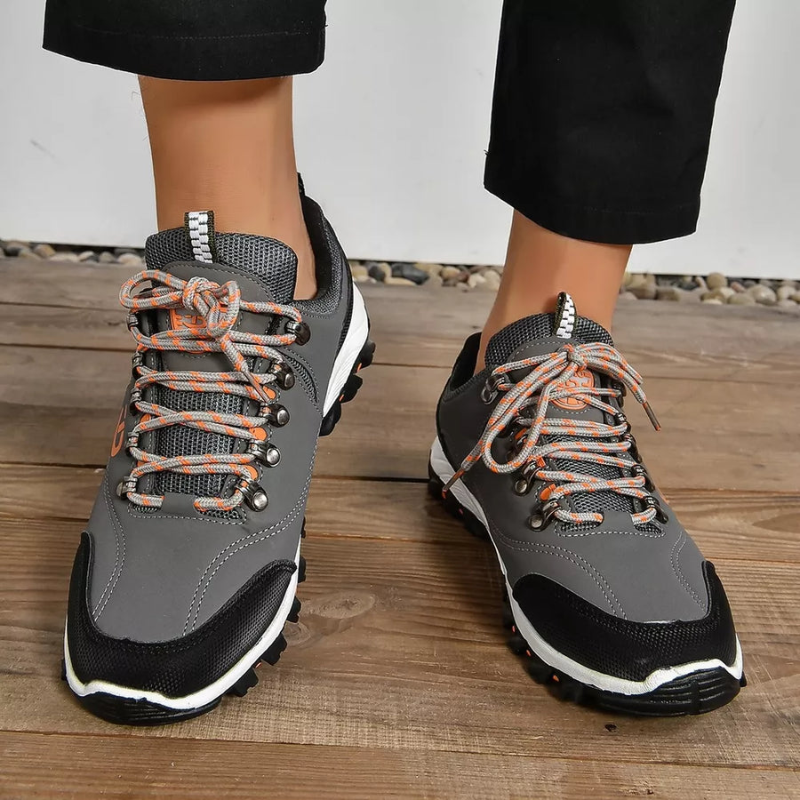 Grey lace-up low-top sneakers with patterned orange and grey laces and black toe caps.