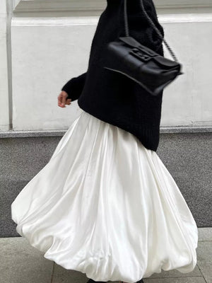 White satin maxi skirt with voluminous balloon hem, paired with a black textured sweater and handbag.