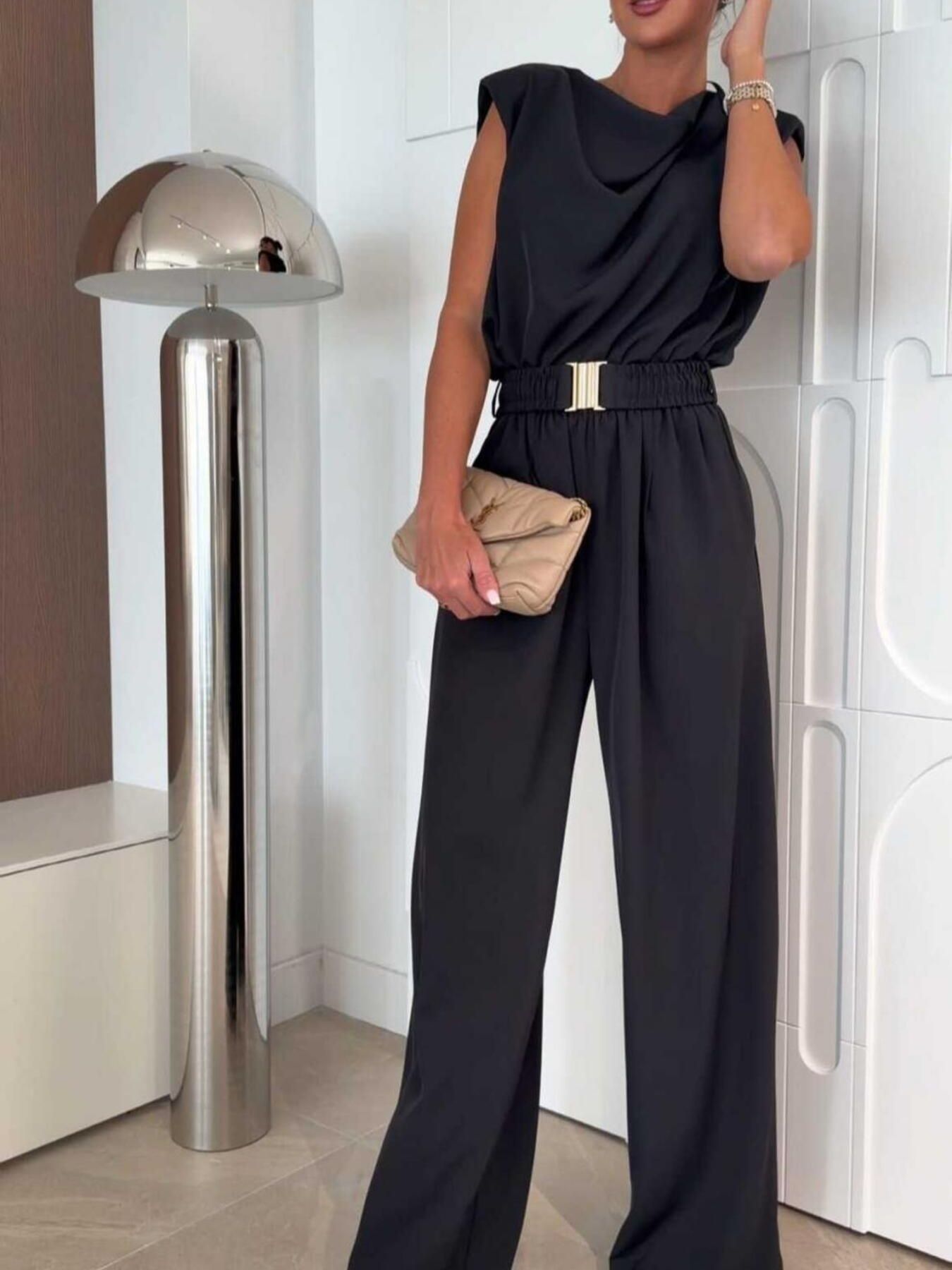 Black wide-leg jumpsuit with cowl neck, sleeveless design, and gold buckle belt.