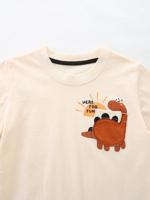Cream cotton baby t-shirt with a brown dinosaur graphic and "HERE FOR FUN" text.