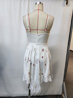 White floral lace trim cami dress with adjustable straps and a ruffled hem.