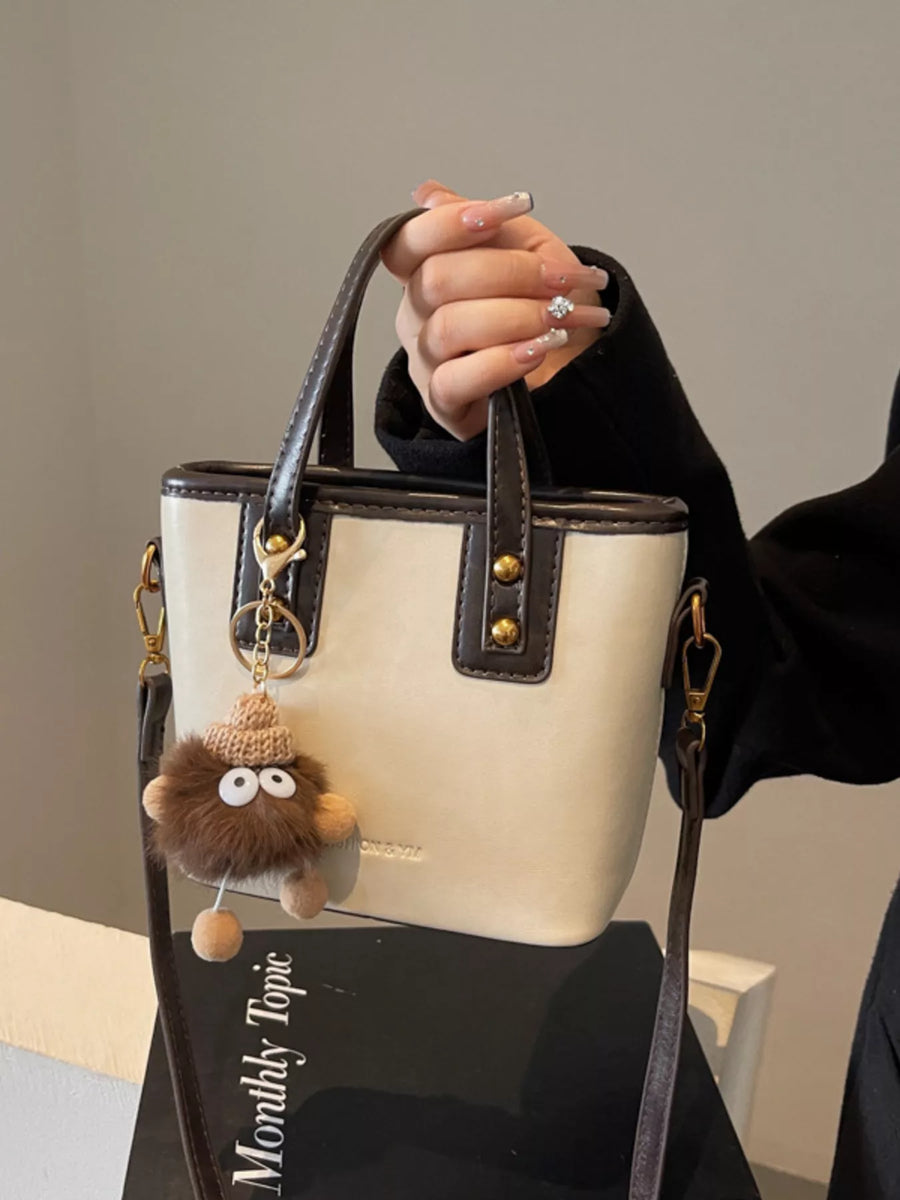 Mini leather crossbody bag in beige with brown trim and a fuzzy charm.