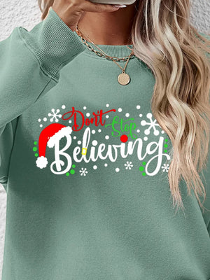 Sage green long sleeve sweater with "Don't Stop Believing" graphic and Santa hat detail.