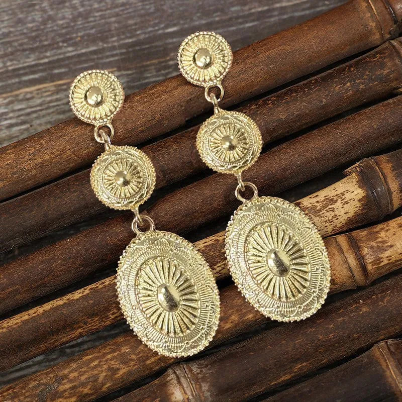 Gold sunburst drop earrings with oval and round embossed details.