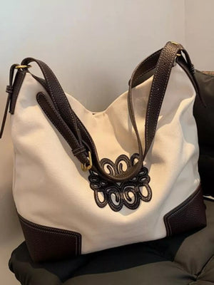White canvas tote bag with dark brown leather trim and embroidered detail