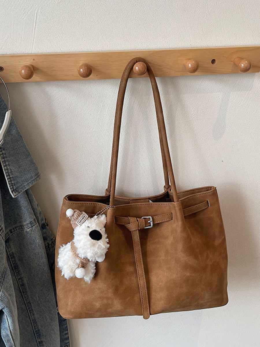 Brown shoulder bag with buckle accent and decorative strap, featuring a fluffy dog charm.