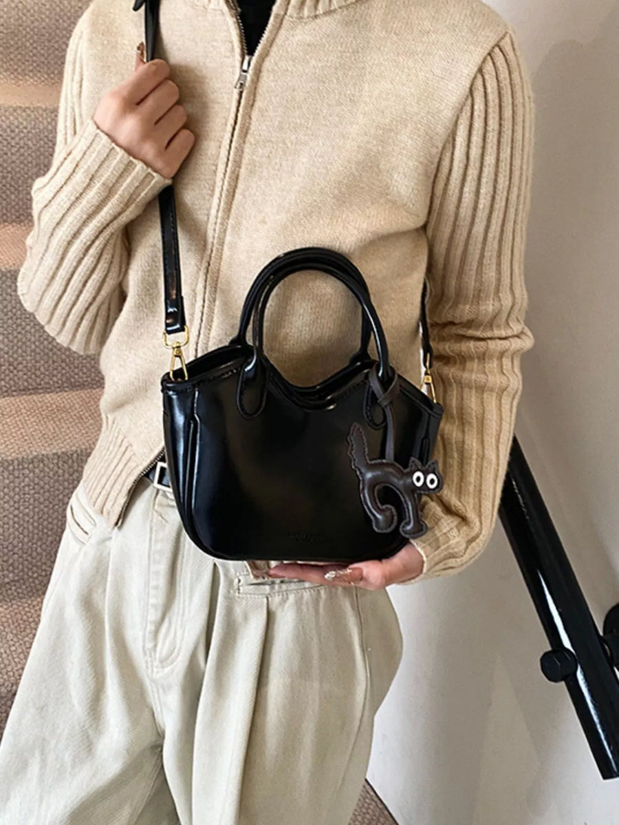 Black mini crossbody bag with a playful cat charm accessory.