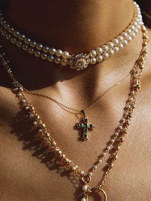 Emerald & Zirconia Cross Pendant necklace with gold chain and pearl accents.