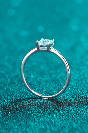 Silver ring with a square cut moissanite stone on a teal glitter background.