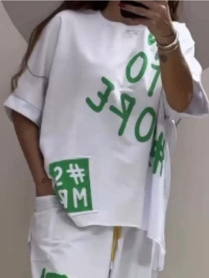 White graphic tee with green text and patches, paired with drawstring pants.