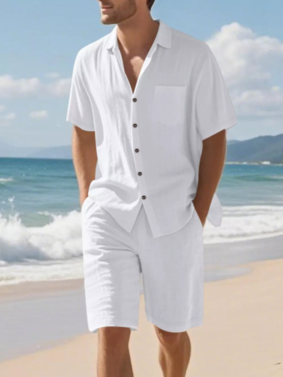 Men's white short sleeve button-up shirt and shorts ensemble on beach.
