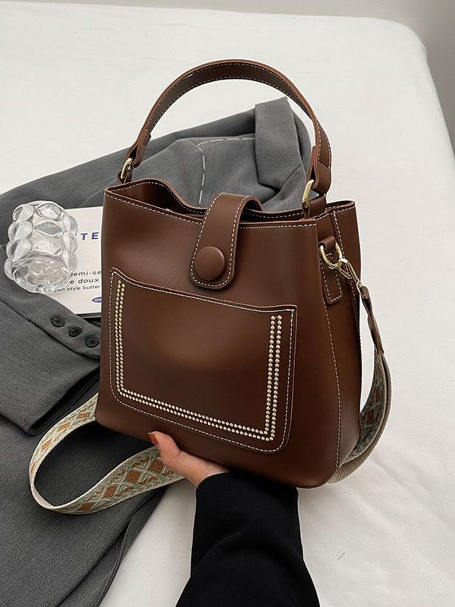 Brown pu leather bucket crossbody bag with decorative stitching and button closure.