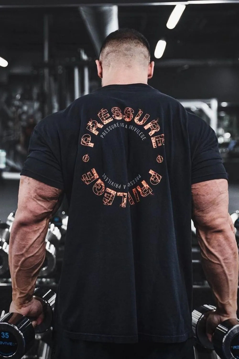 Black graphic t-shirt with circular "Pressure Privilege" text and dumbbell icons.