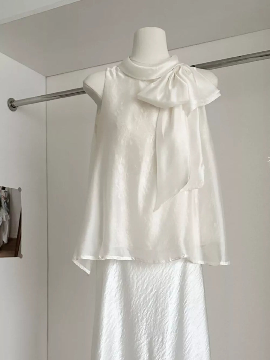 Sleeveless white shirt with a large bow detail on the shoulder and a textured fabric.