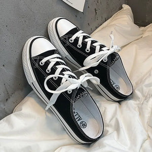 Black canvas mule sneakers with white contrast trim and laces.