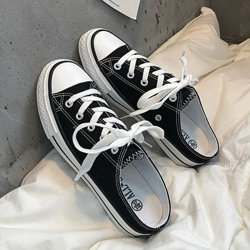 Black canvas mule sneakers with white contrast trim and laces.