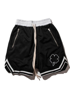 Black mesh basketball shorts with drawstring, zipper pockets, and clover detail.