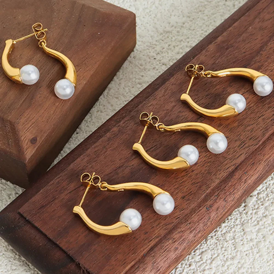 Gold sculptural pearl drop hoop earrings with a modern curved design.