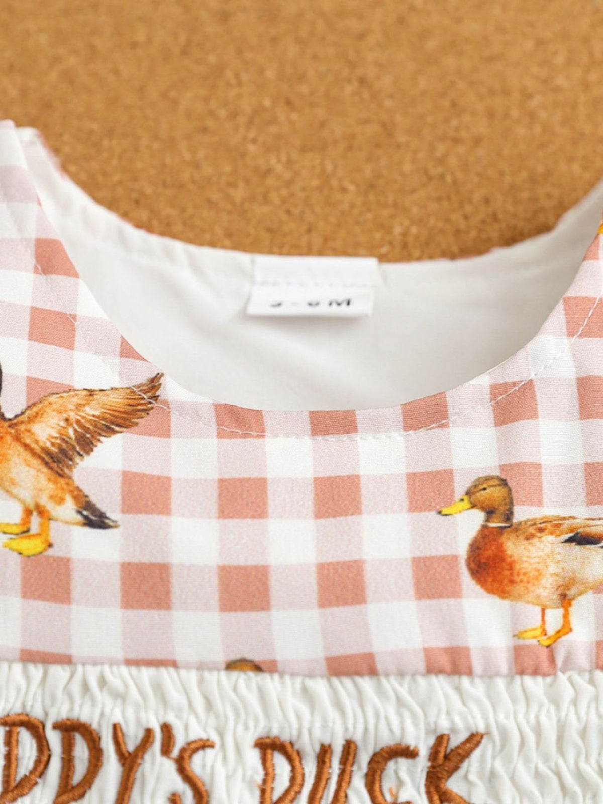Baby one-piece with duck print on pink gingham, smocked waist, and embroidered text.