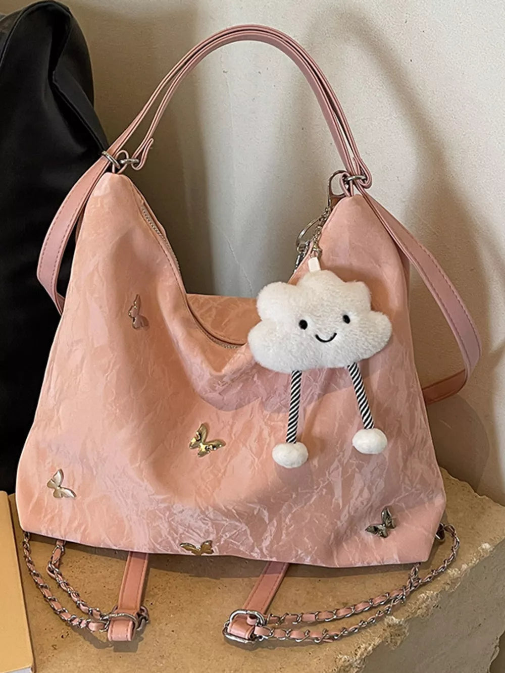 Blush pink shoulder bag with butterfly embellishments and a cloud charm.