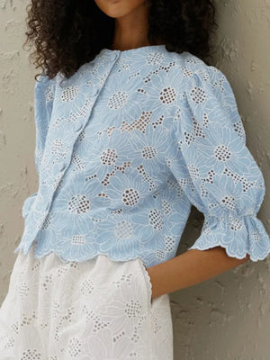 Blue eyelet blouse with floral embroidery, puff sleeves, and ruffled cuffs.