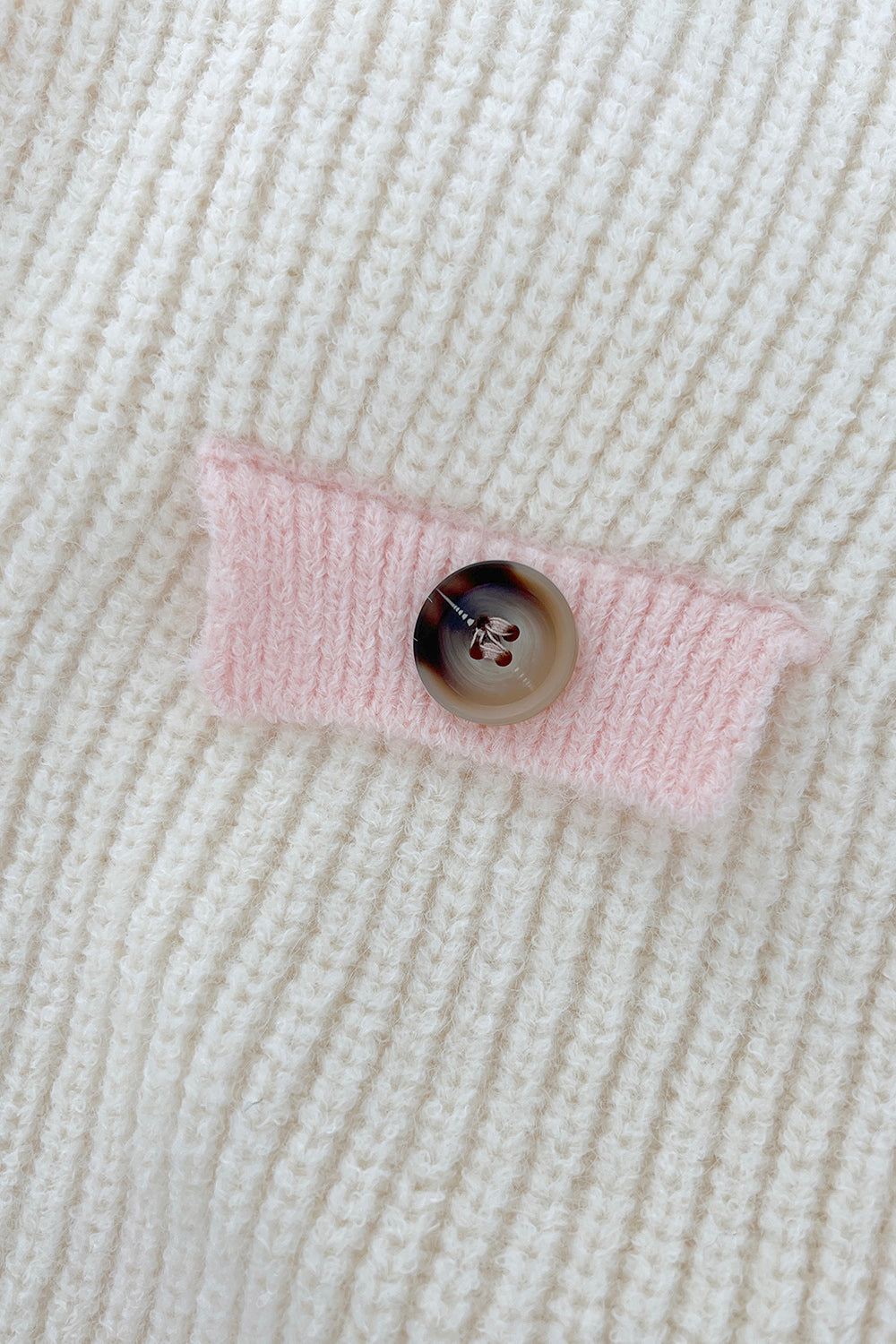 Cream knit cardigan with pink trim detail and button closure.
