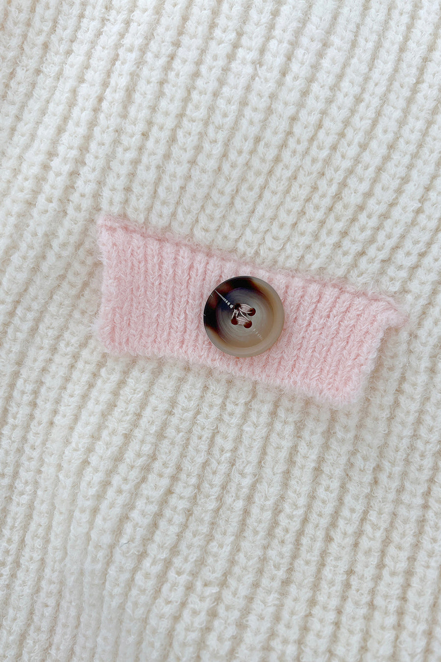 Cream knit cardigan with pink trim detail and button closure.