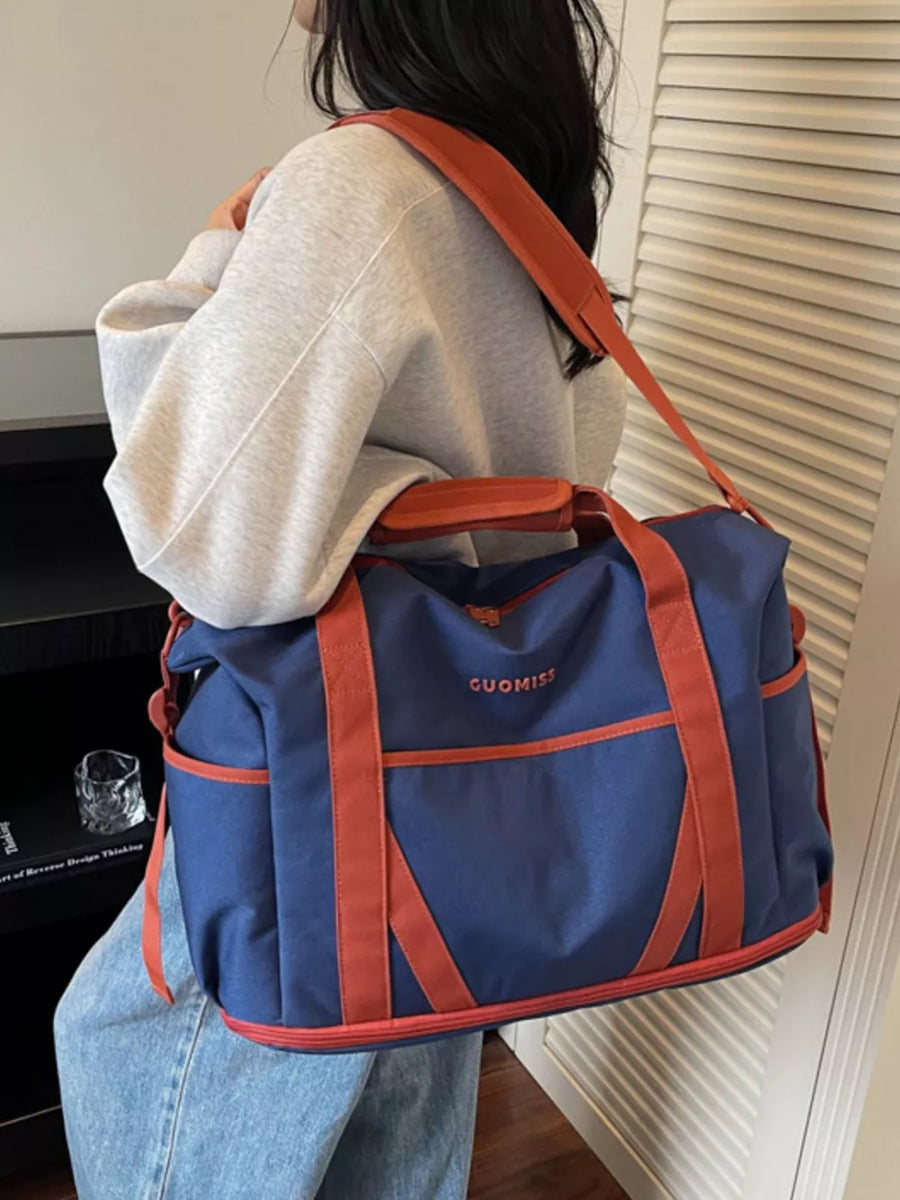 Blue duffel bag with orange trim and strap, featuring a logo and side pockets.