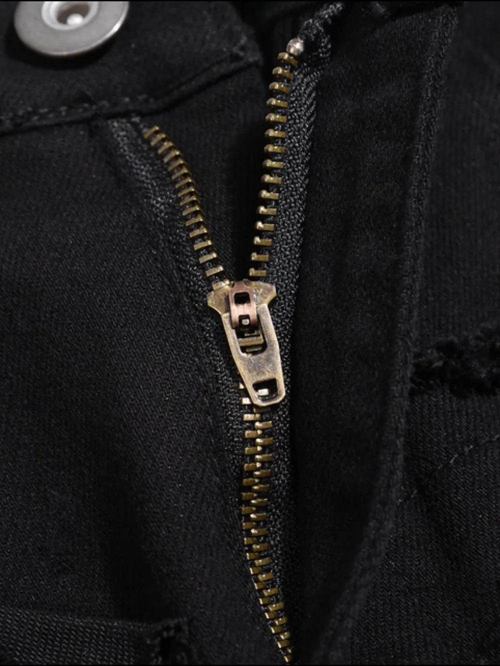 Black denim jeans with frayed edges and a brass zipper detail.