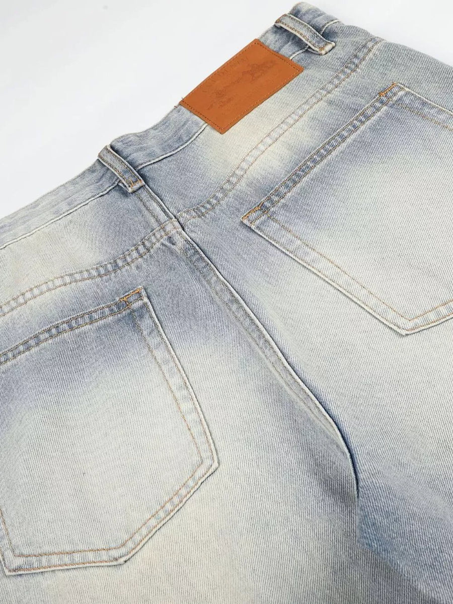 Men's light wash vintage denim jeans with wide leg and brown leather back patch.