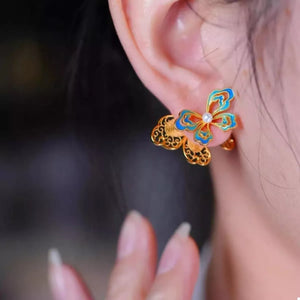 Gold butterfly stud earrings with blue enamel and pearl detail.