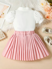 Girls' pink pleated skirt with a white puff-sleeve top, bow detail.